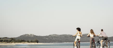 Three people on bicycles by a waterfront with a hilly landscape in the background.