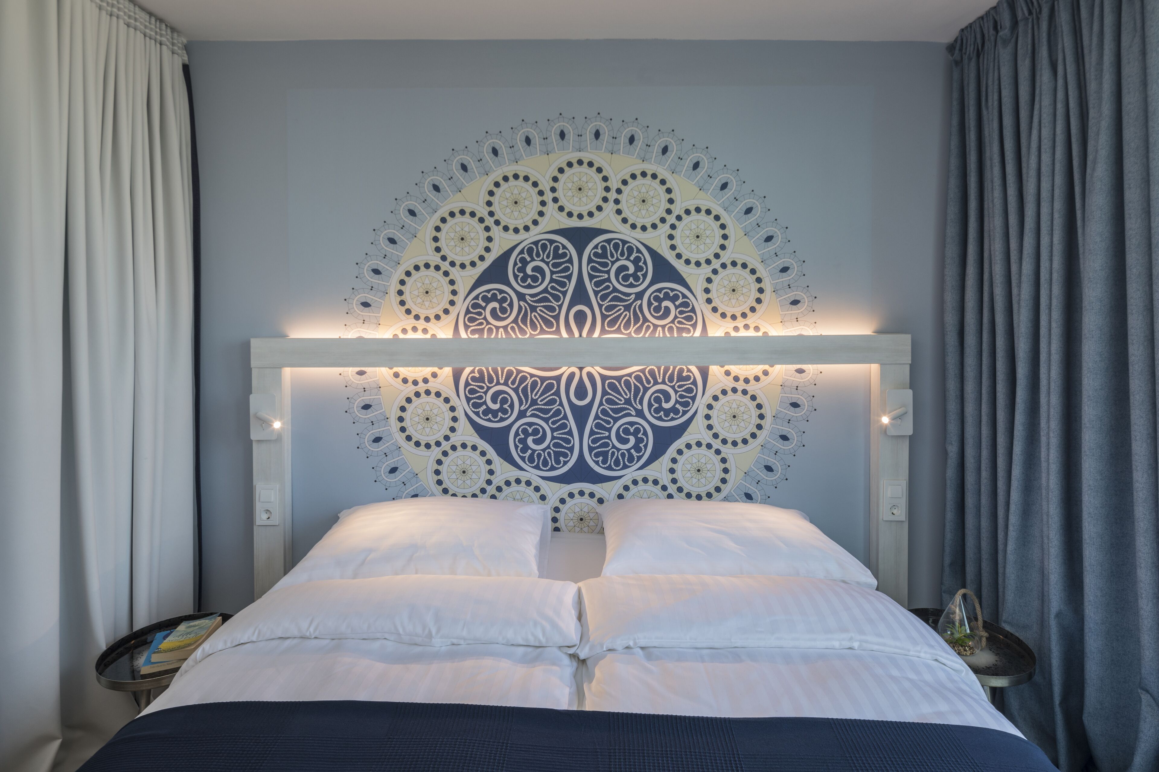A neatly made bed with a decorative headboard, a bedside table with a book, and a nightstand with a lamp.