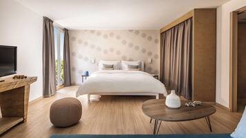 A modern hotel room with a large bed, a TV, a wooden desk, and a round table.