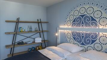 A bedroom with a bed, a headboard with a decorative pattern, wooden shelves with various items, and a wall tapestry.