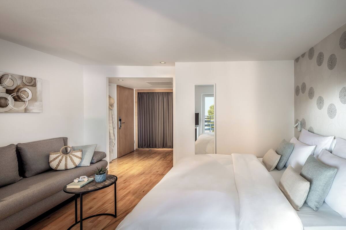 A modern hotel room with a sofa, a bed, a small table, and a wall with circular patterns.
