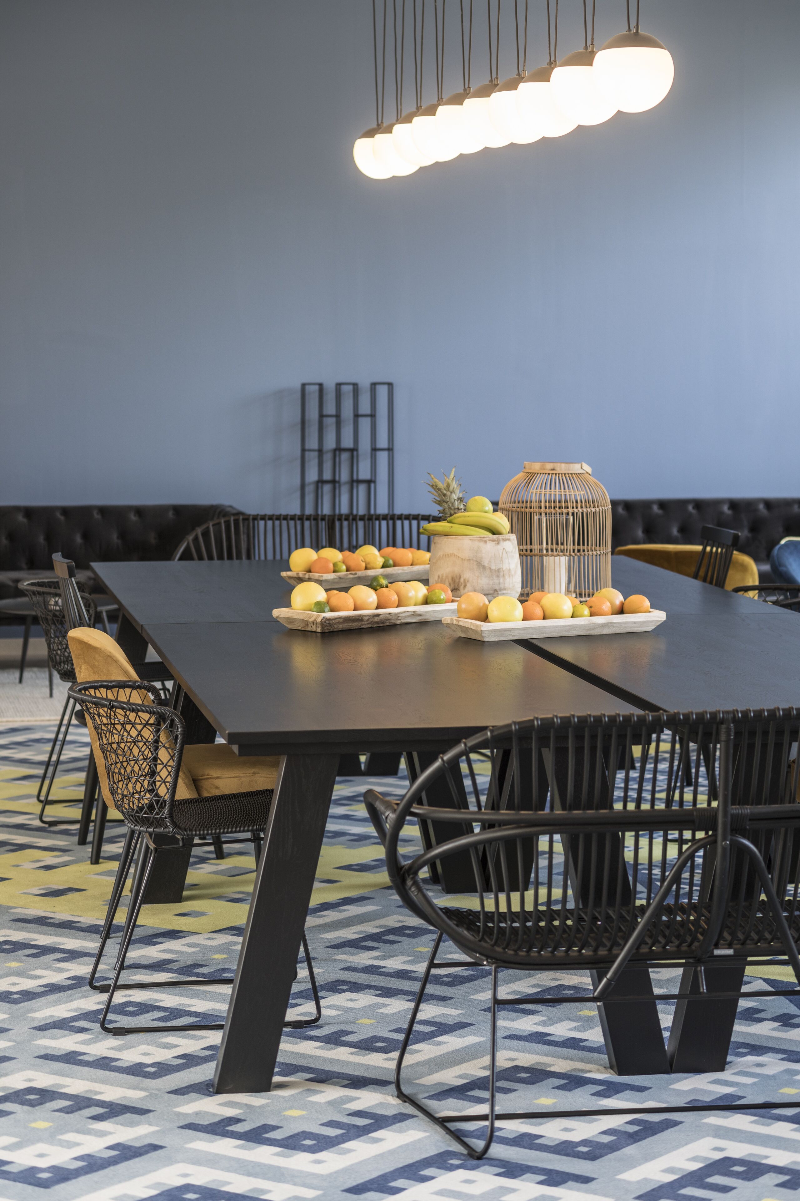 Un comedor con una mesa larga, sillas negras y una exhibición de frutas.