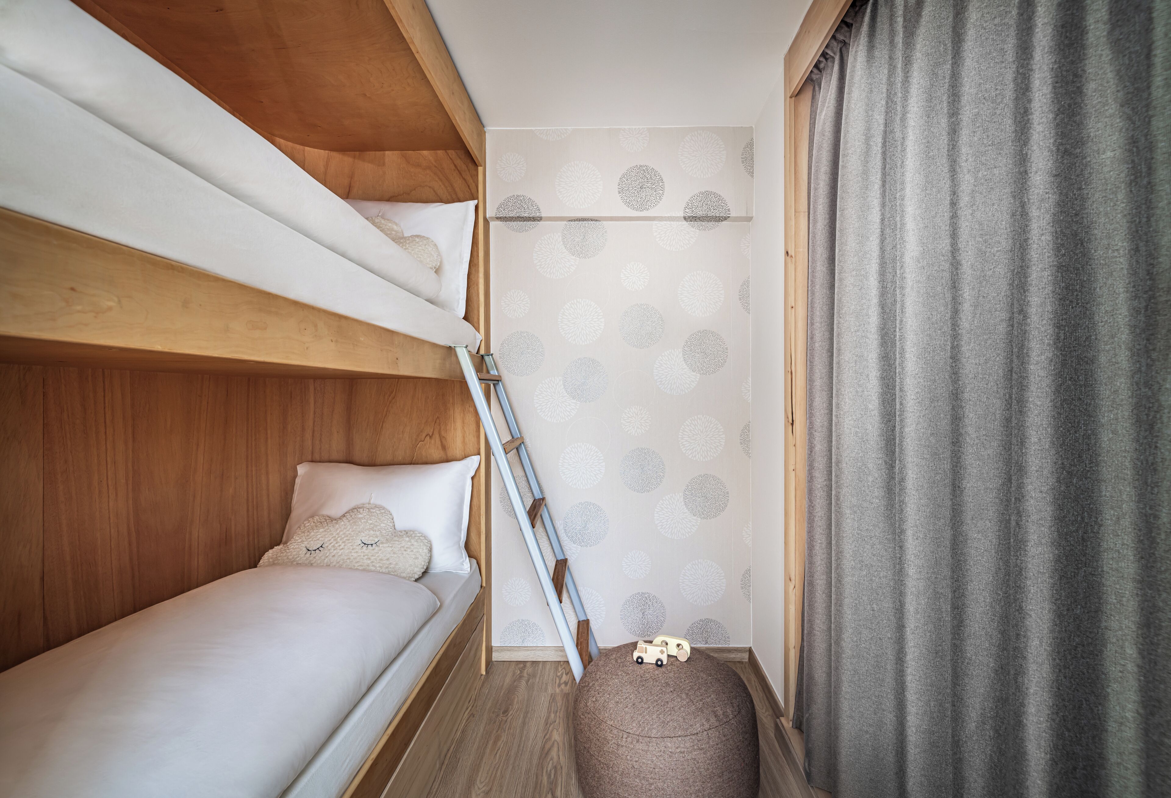 Un dormitorio pequeño con una cama litera, un pequeño reposapiés y un coche de juguete.