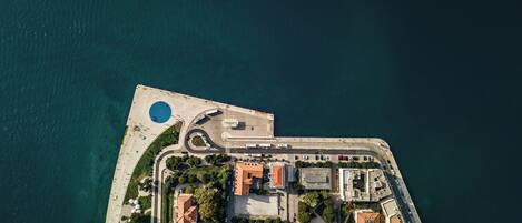 An aerial view of a coastal area with a marina, a roundabout, and buildings with red-tiled roofs.