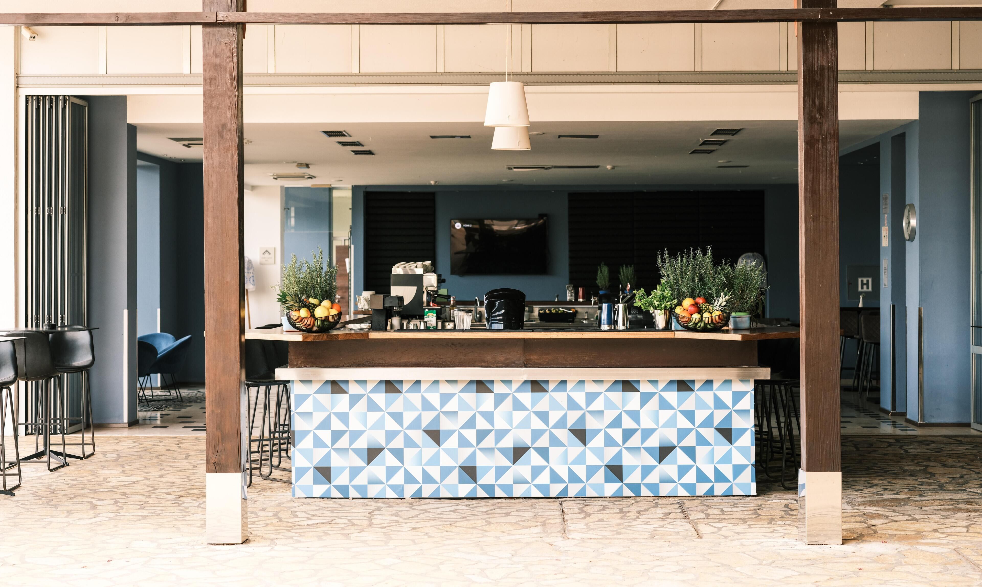 An outdoor bar area with a patterned counter, seating, and a television screen in the background.