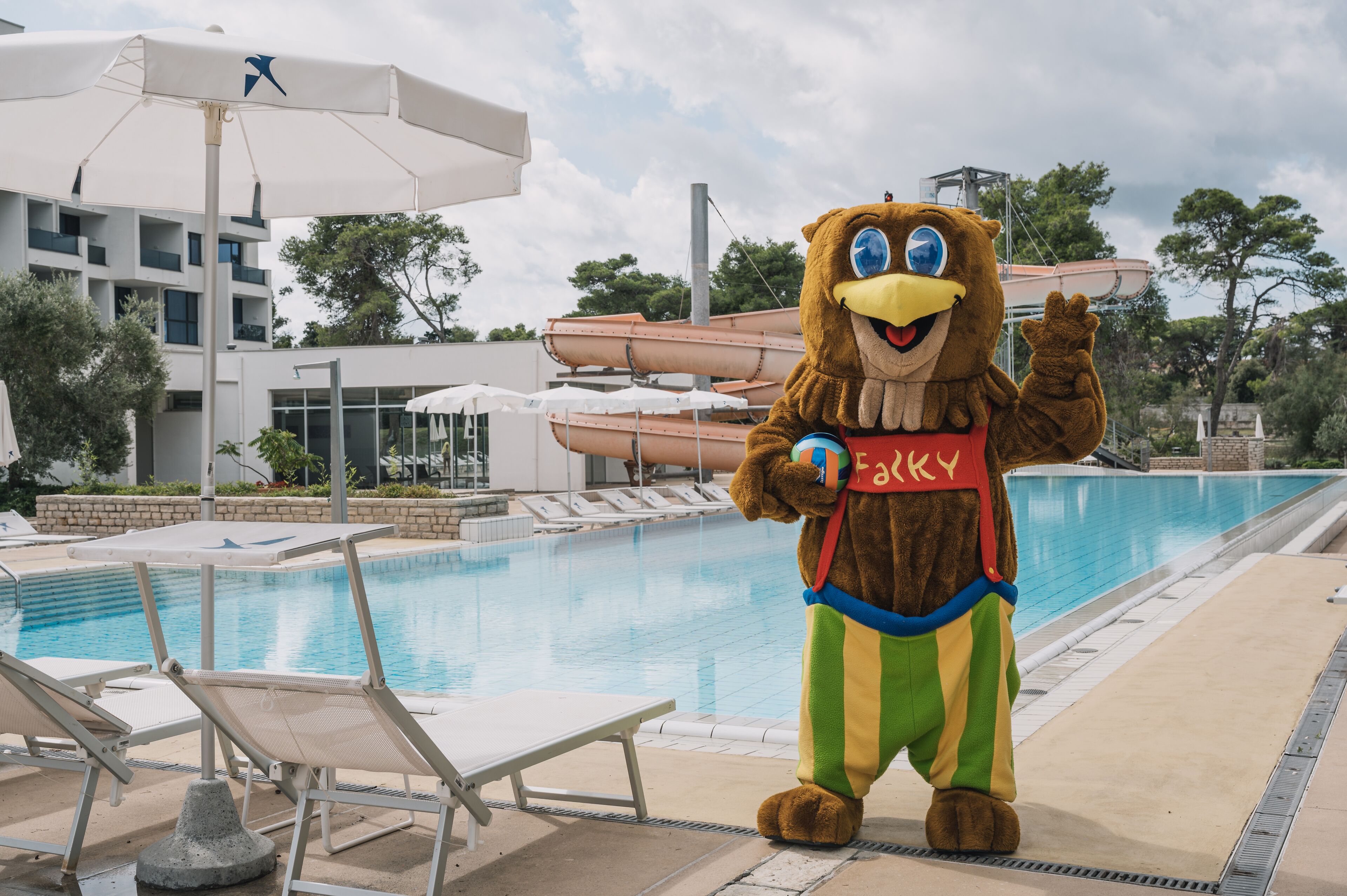 A mascot near a pool with lounge chairs and umbrellas.
