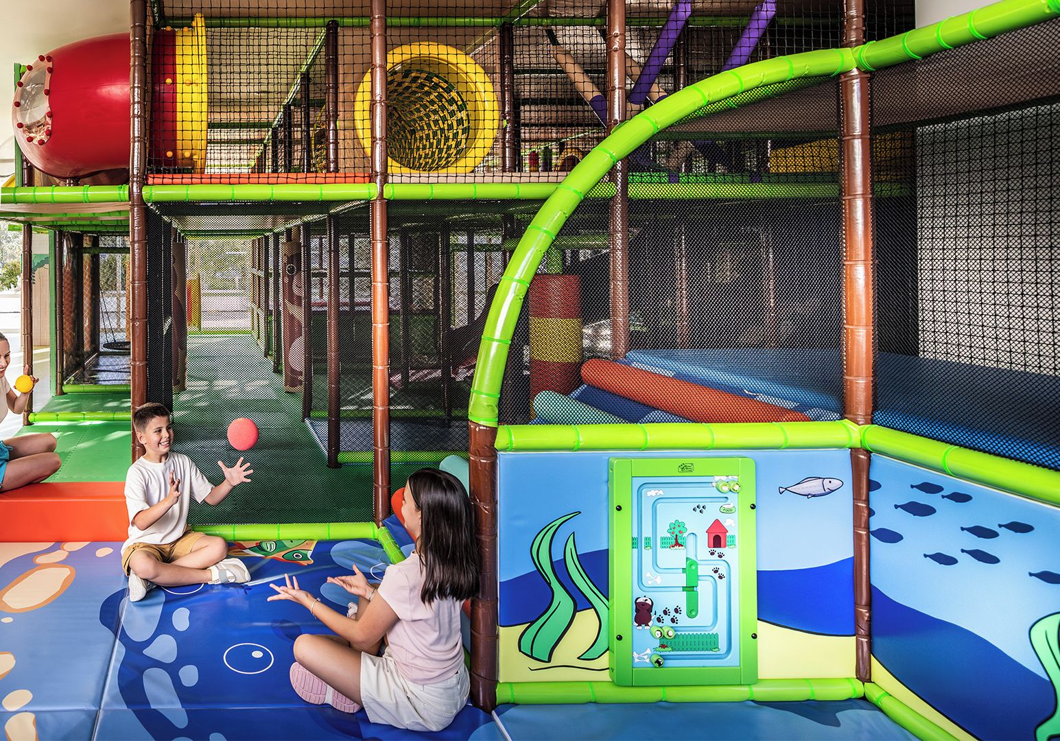 A children's playground with netted climbing structures, a slide, and a play area with a starfish decoration.