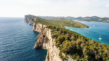 A coastal landscape with cliffs, clear turquoise waters, and sailboats.
