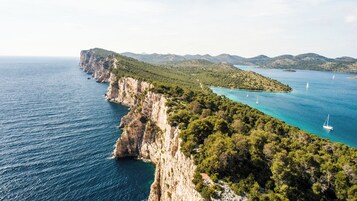 A coastal landscape with cliffs, clear turquoise waters, and sailboats.
