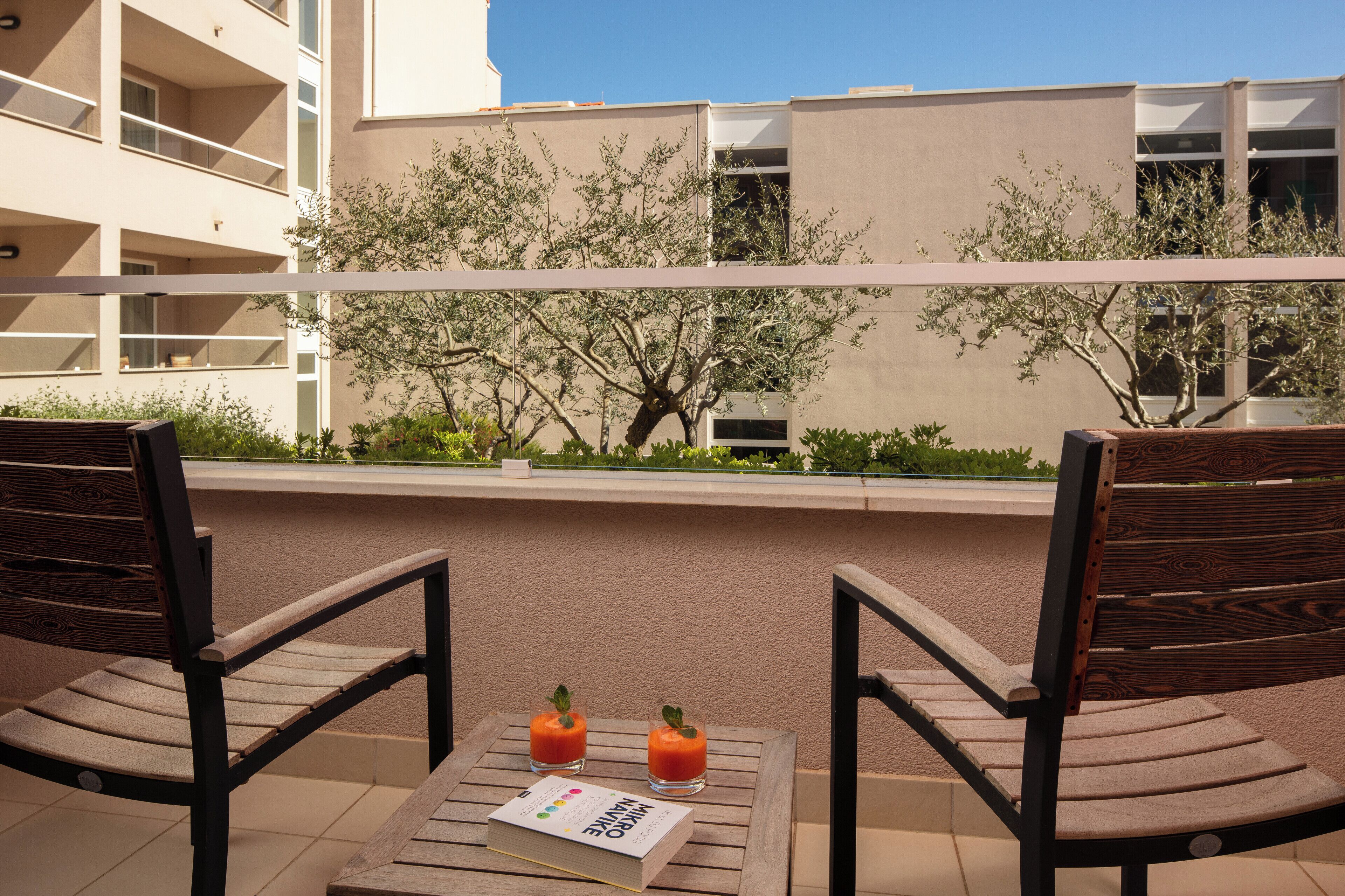 Un balcon avec deux chaises en bois, une table et deux boissons.