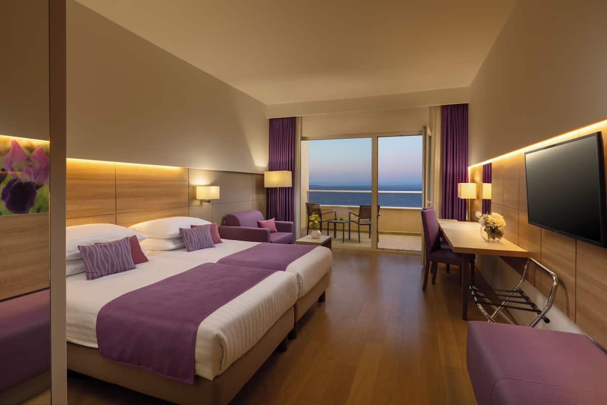 Habitación de hotel con una cama grande, un escritorio y vistas al mar.
