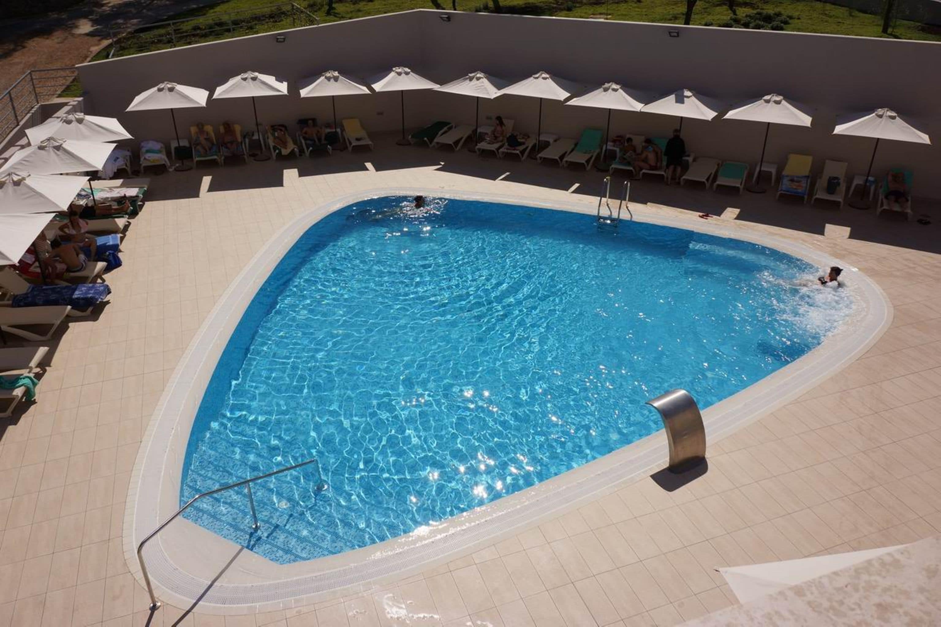 Une piscine dont le fond est recouvert de carrelage, entourée de chaises longues et de parasols.