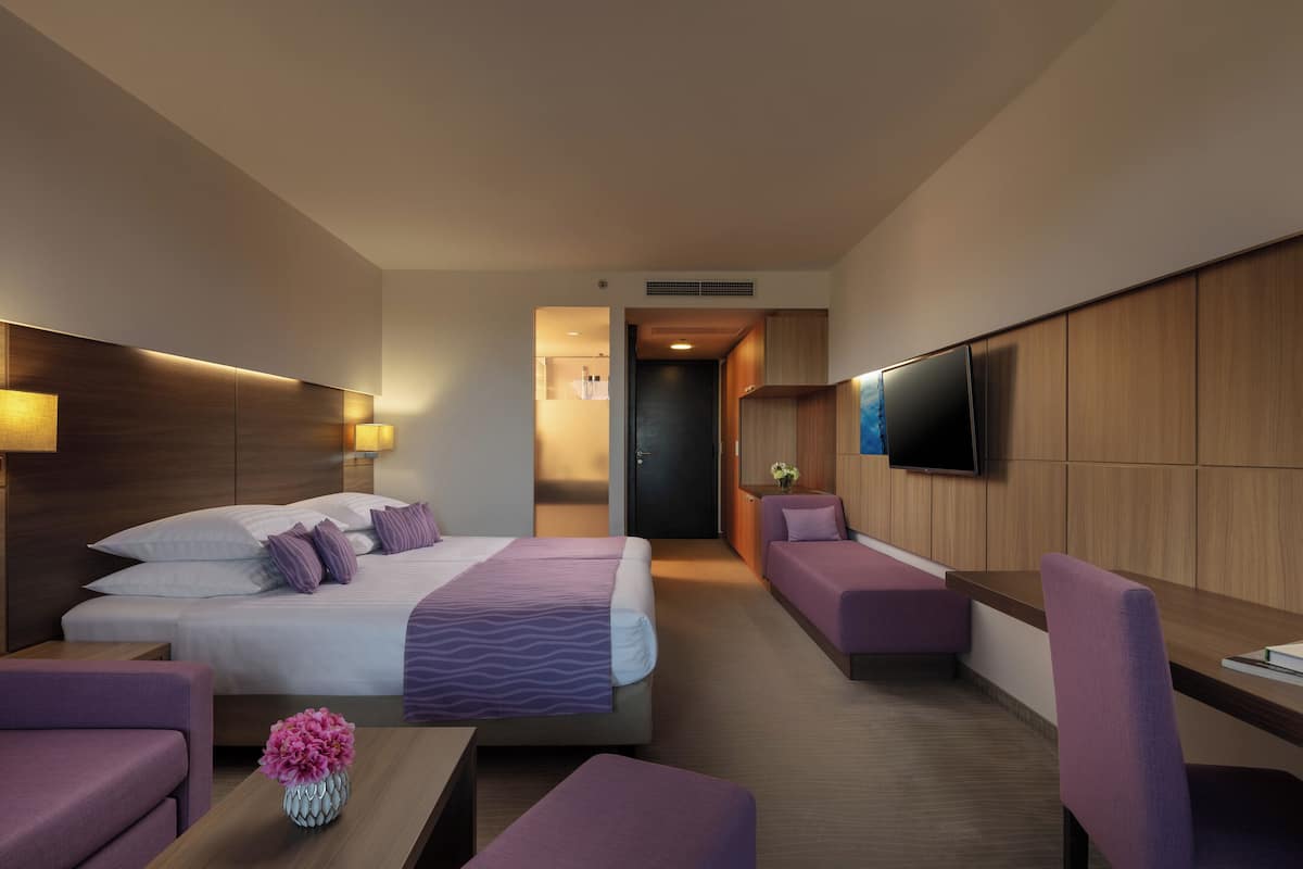 Una habitación de hotel moderna con una cama grande, un escritorio, un sofá y un televisor montado en la pared.