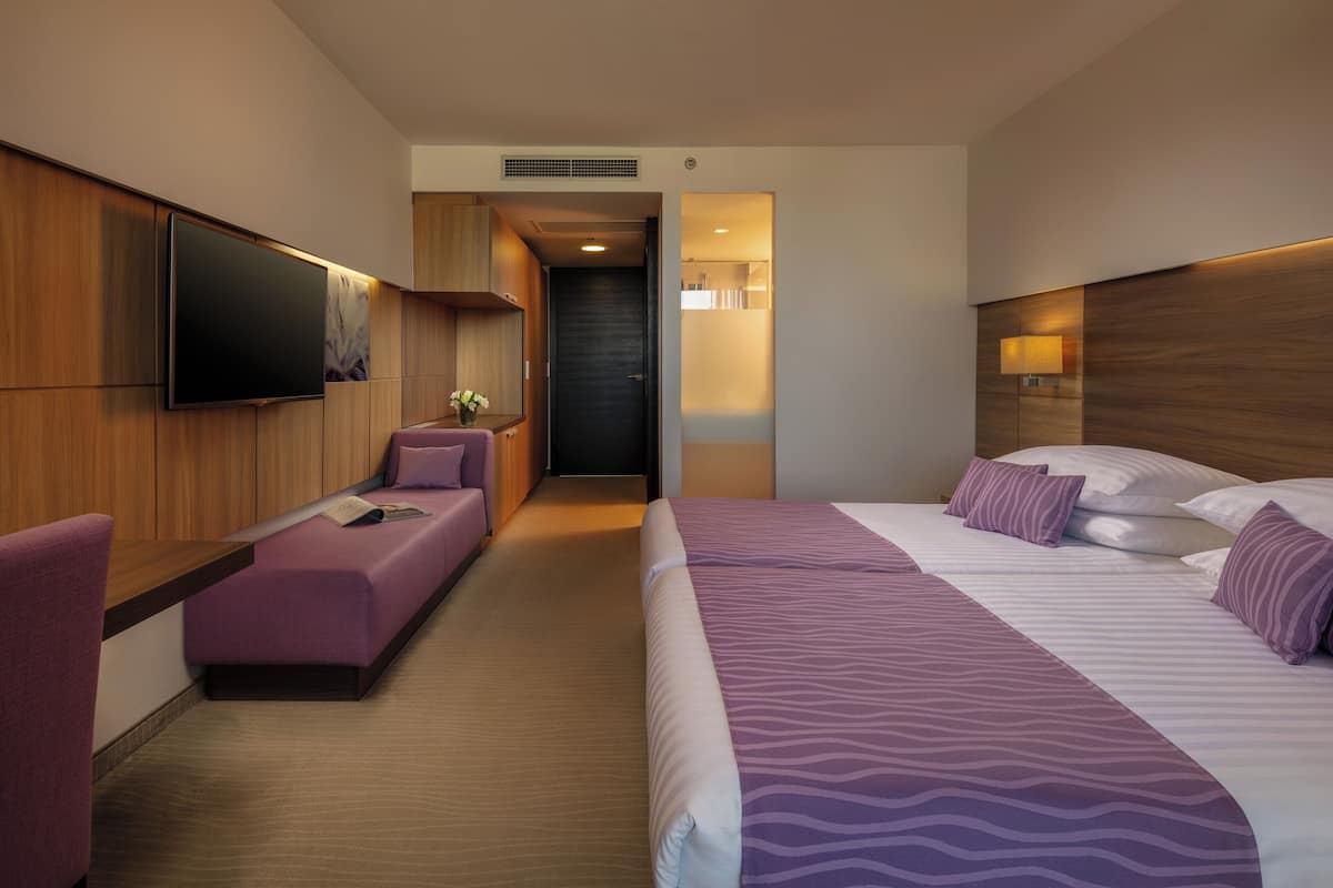 Una habitación de hotel moderna con una cama grande, un sofá, un televisor montado en la pared y una mesita.
