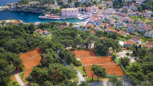 Vista aérea de un pueblo costero con un puerto deportivo, canchas de tenis y edificios residenciales.