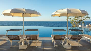 Una piscina a sfioro con sedie a sdraio e ombrelloni, con vista sul mare.