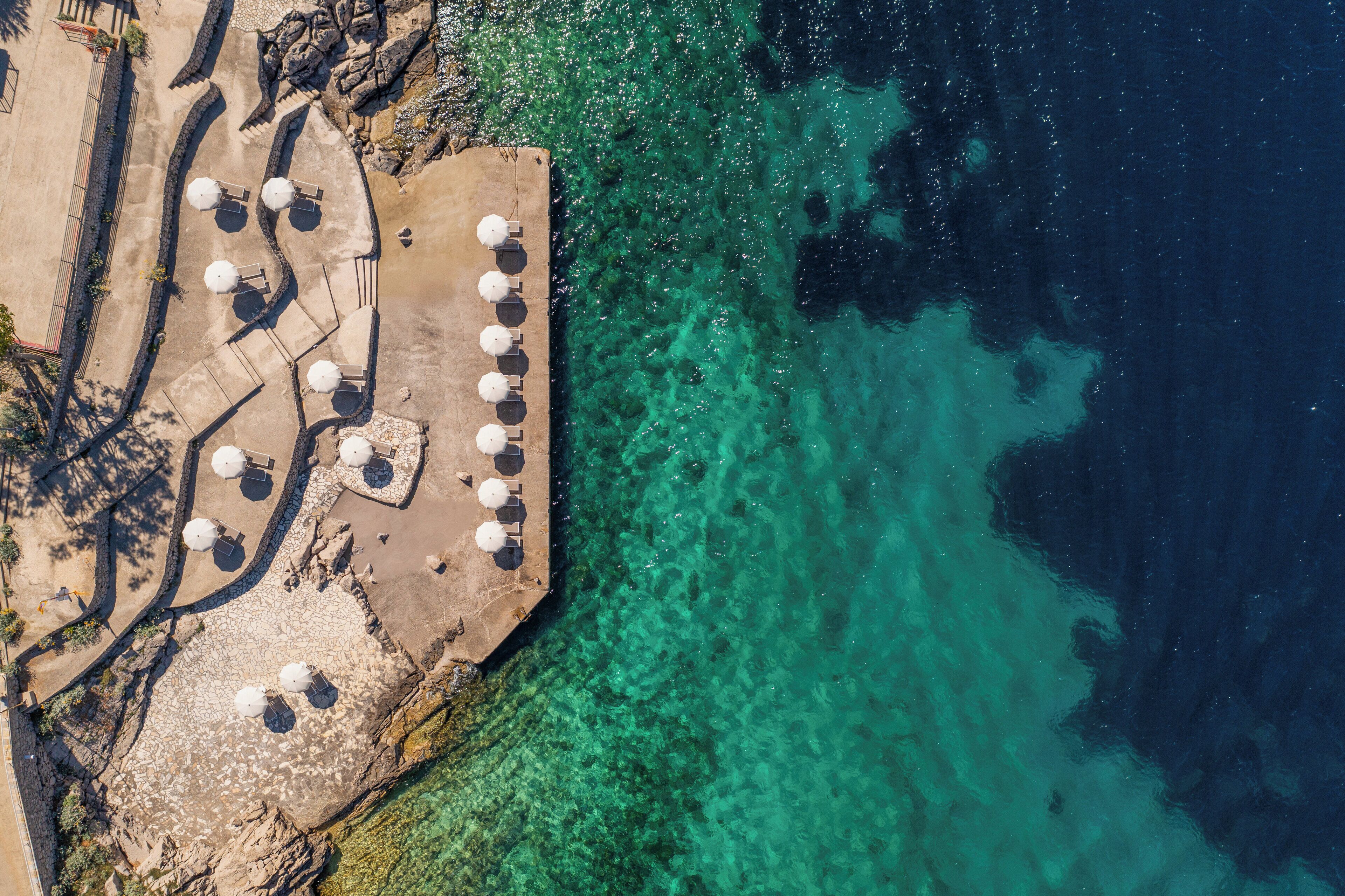 An aerial view of a coastal area with a concrete platform featuring multiple umbrellas and seating arrangements.