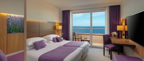 A hotel room with a large bed, a desk, a chair, and a view of the sea.