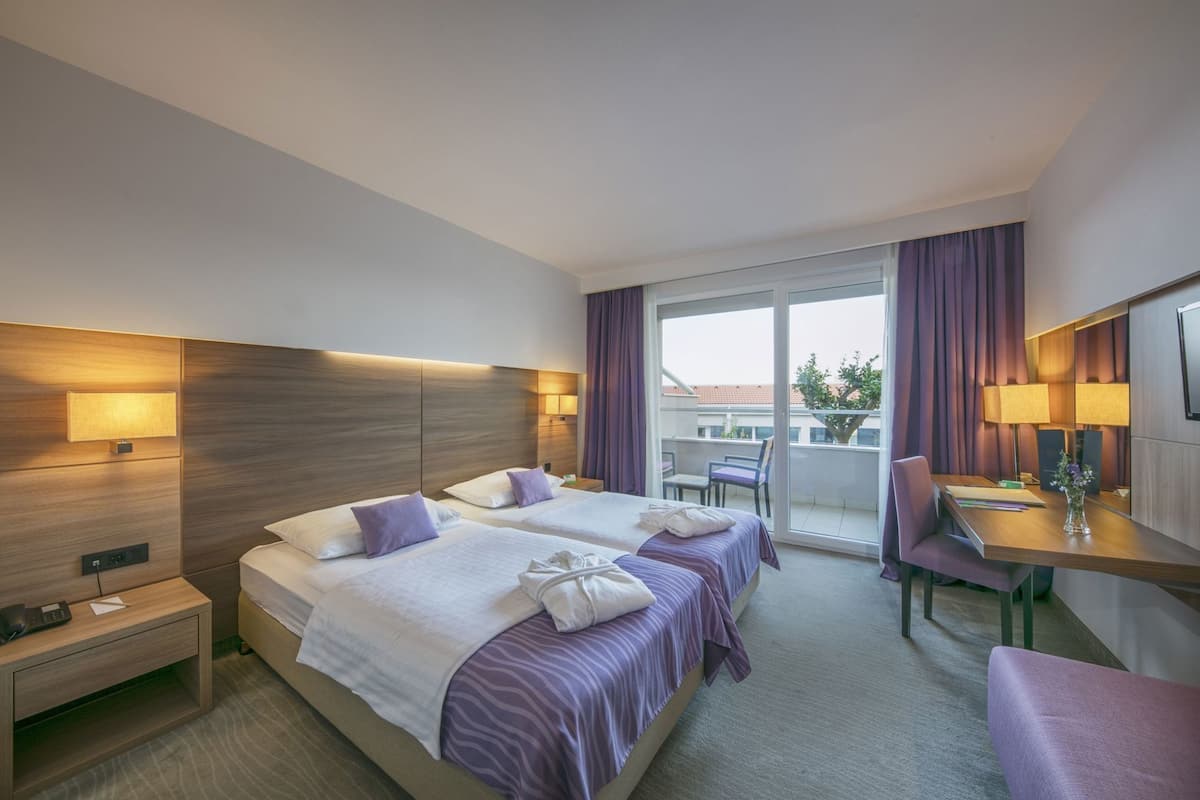 Habitación de hotel con dos camas, un escritorio, una silla, un balcón con vistas y un televisor.