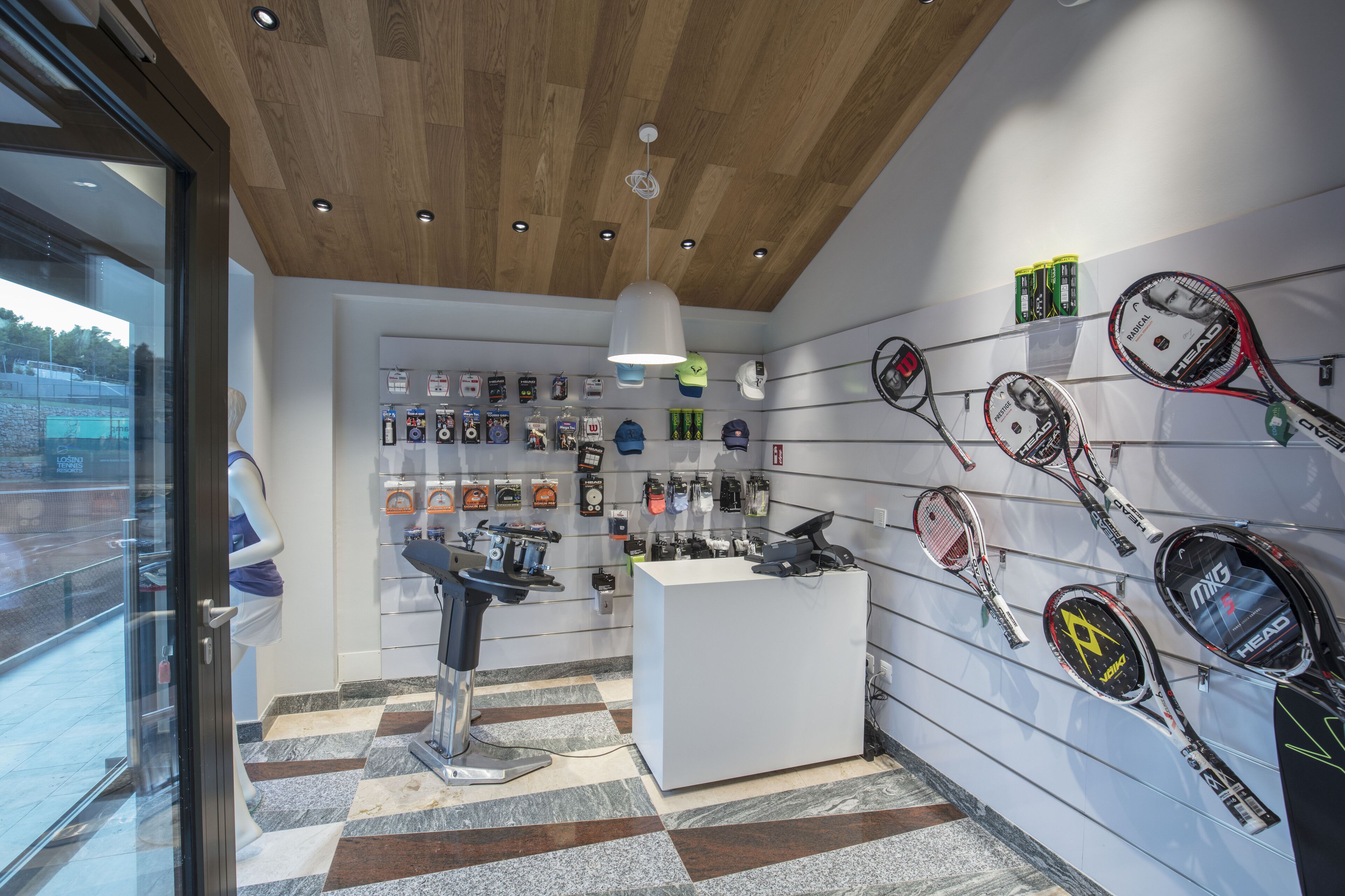 Una tienda de artículos deportivos que exhibe una variedad de equipos para deportes de raqueta, incluyendo raquetas de tenis y cascos, en sus paredes.