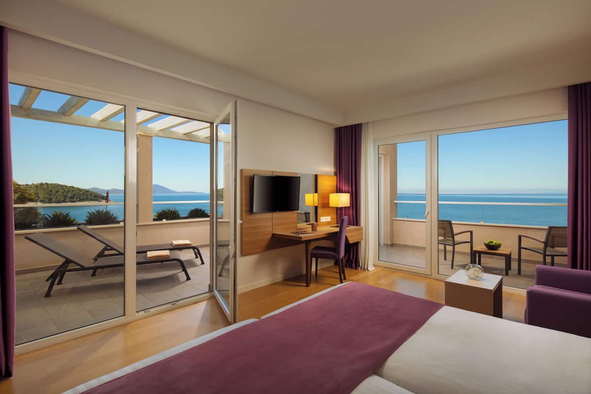 Habitación de hotel con una cama grande, un escritorio con silla, televisión y balcón con vista al mar.