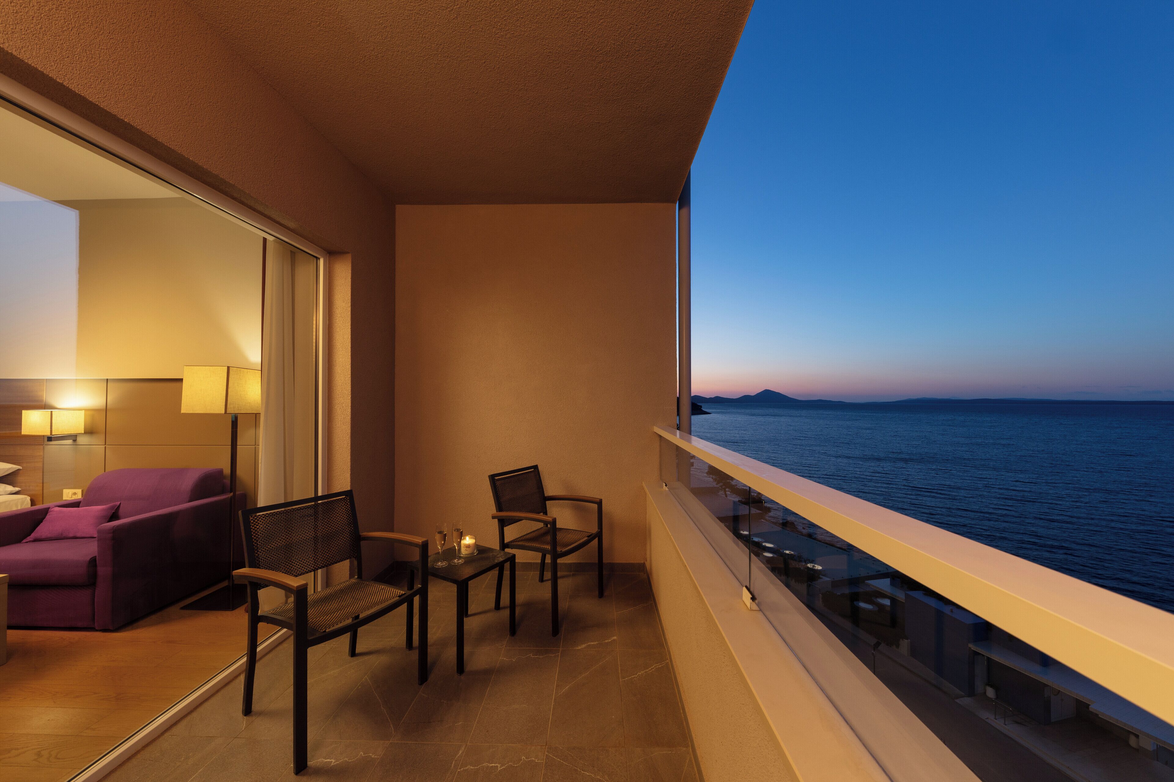 A balcony with a view of the sea, a sofa, two chairs, and a table with a candle.