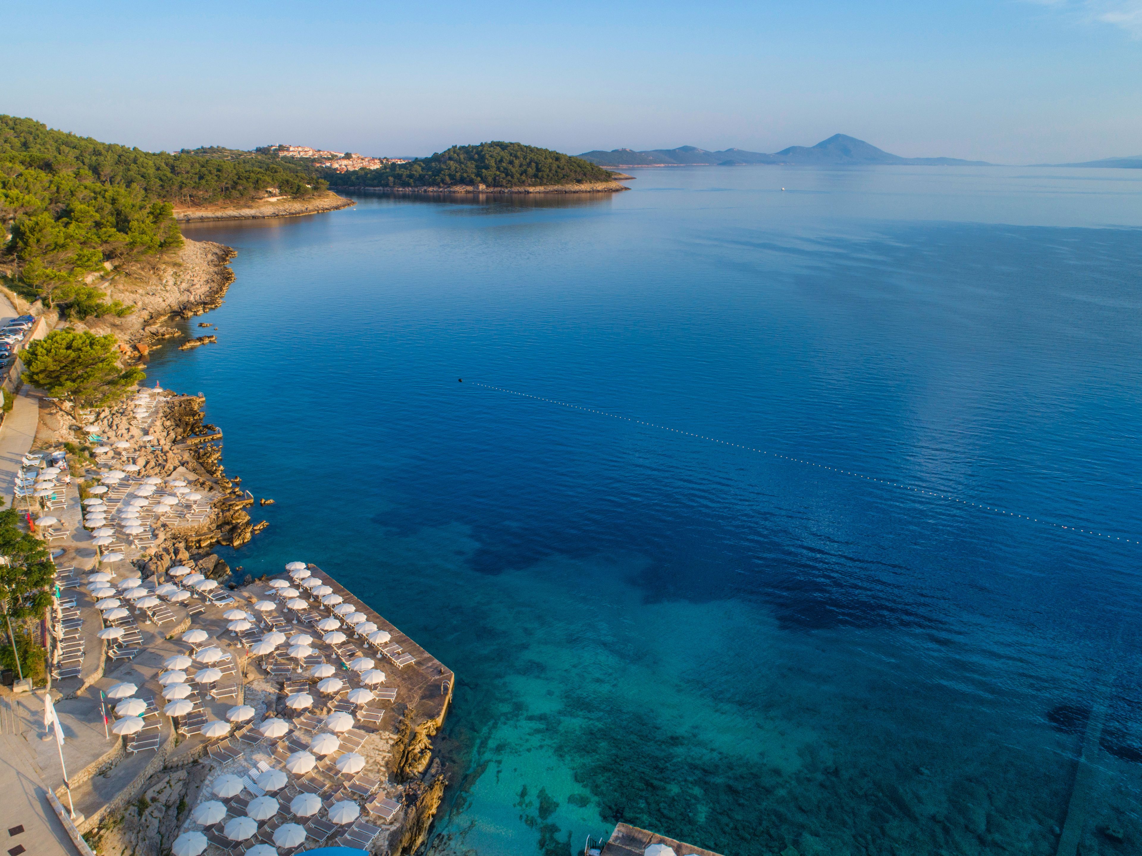 A coastal area with a rocky shoreline, clear blue waters, and a row of beach umbrellas and lounge chairs.