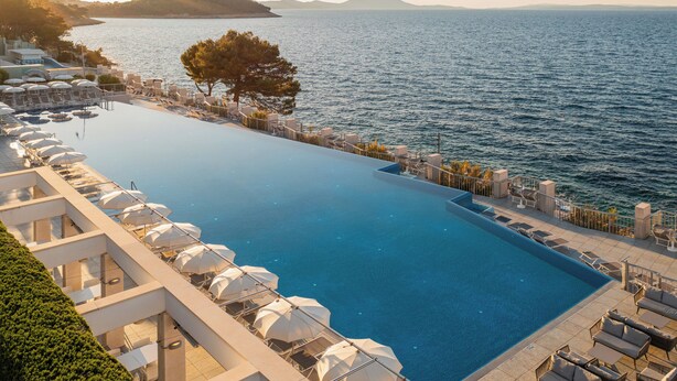 Una amplia piscina infinita con sillones de descanso y sombrillas, con vistas a una masa de agua y una isla distante.
