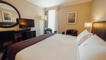 Una camera d'albergo con un letto grande, una scrivania con televisore, una sedia e una lampada.