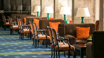 Un vestíbulo de hotel con filas de sillones y sofás, lámparas verdes y una alfombra estampada.