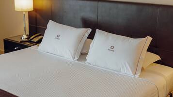 Habitación de hotel con una cama grande, dos almohadas con un logotipo, una lámpara de noche y una mesita de noche con un teléfono.