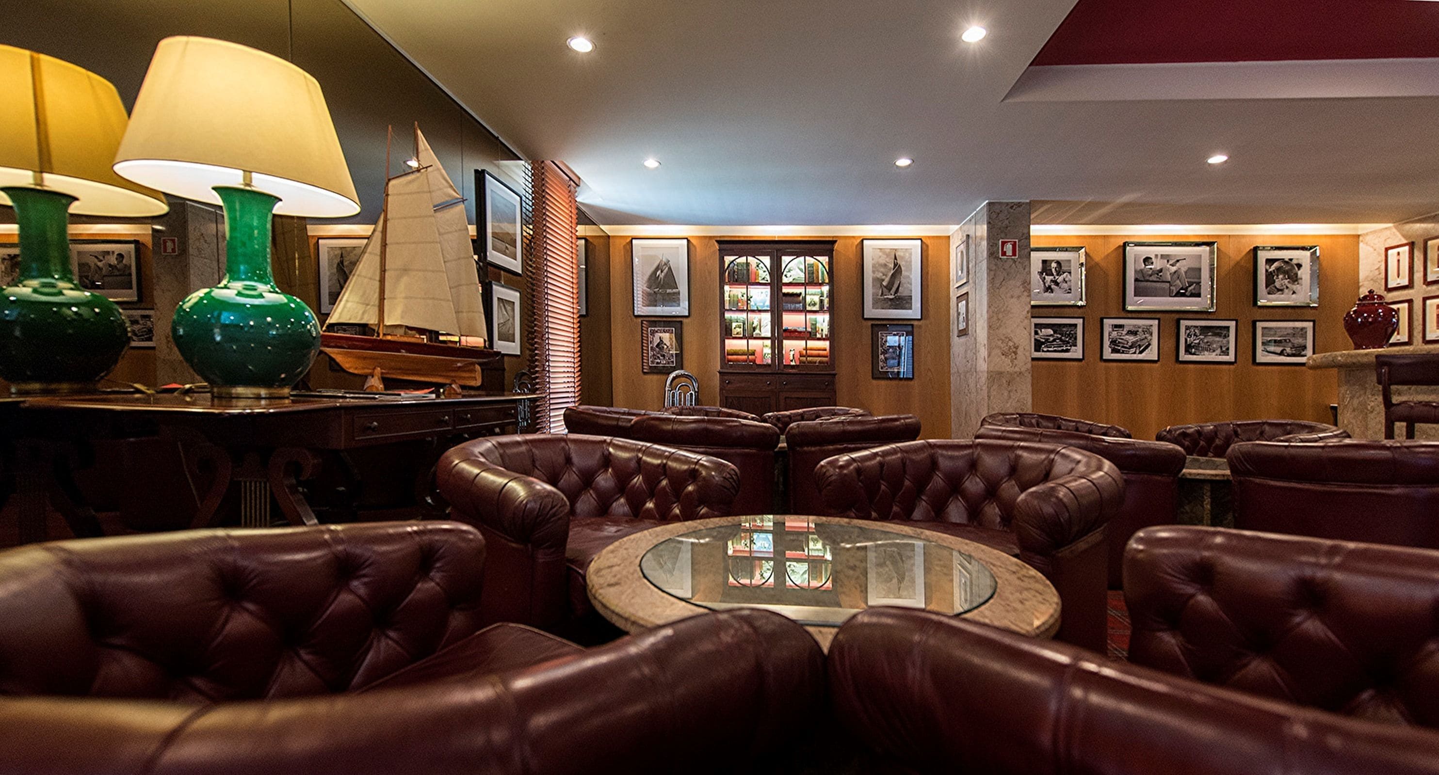 A bar area with leather seating, a round glass table, and framed pictures on the walls.