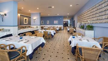 A restaurant with multiple tables, wicker chairs, and a tiled floor.