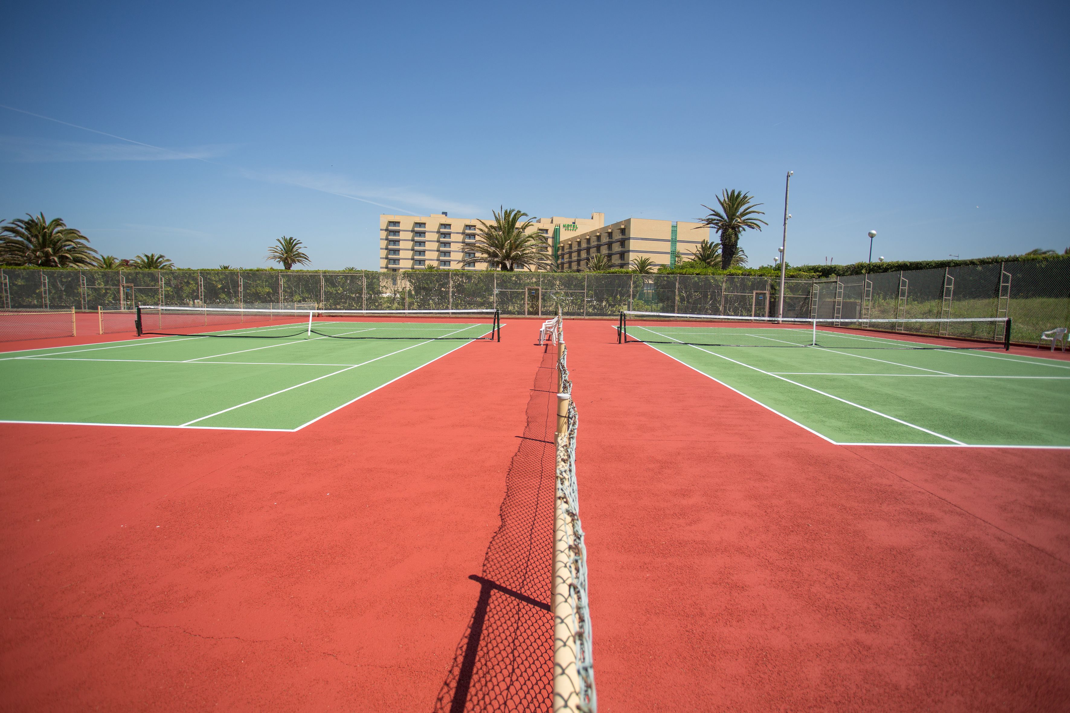 A tennis court with two courts, a net in the middle, and a building in the background.