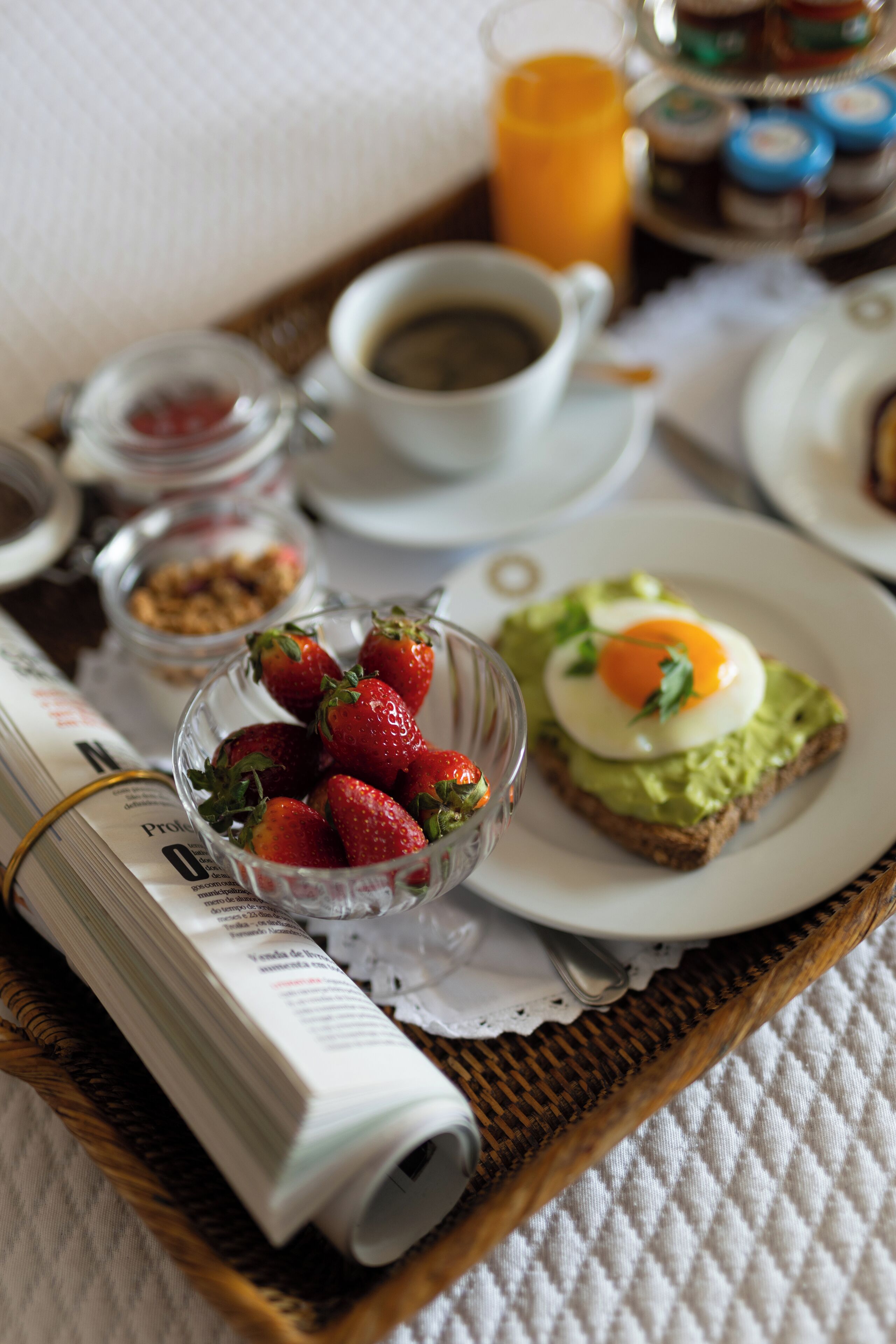 A breakfast tray with a plate of avocado toast, a bowl of strawberries, a cup of coffee, and a glass of orange juice.