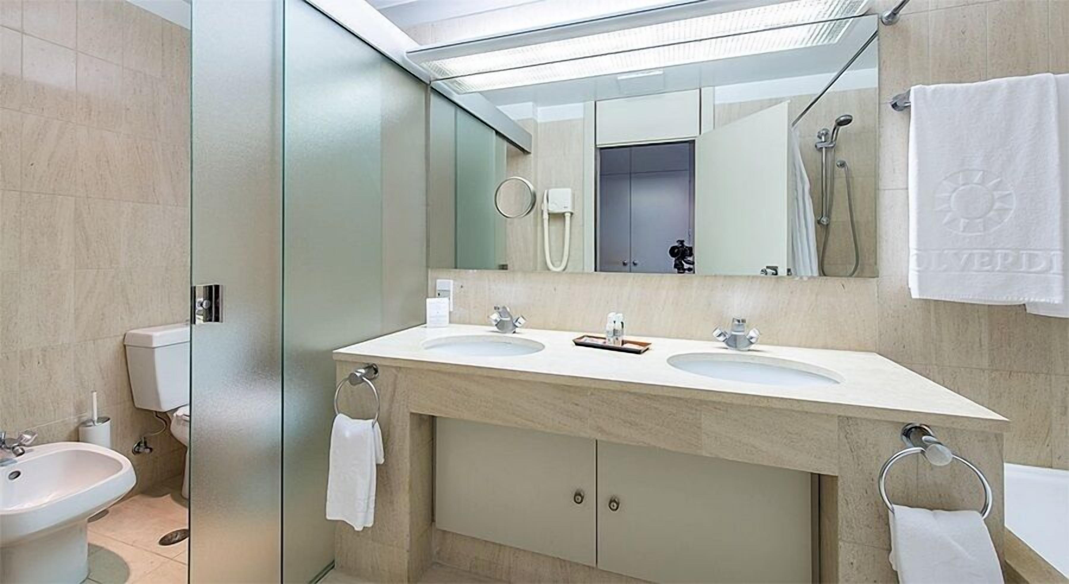 A modern bathroom with two sinks, a large mirror, a towel rack, and a shower area.