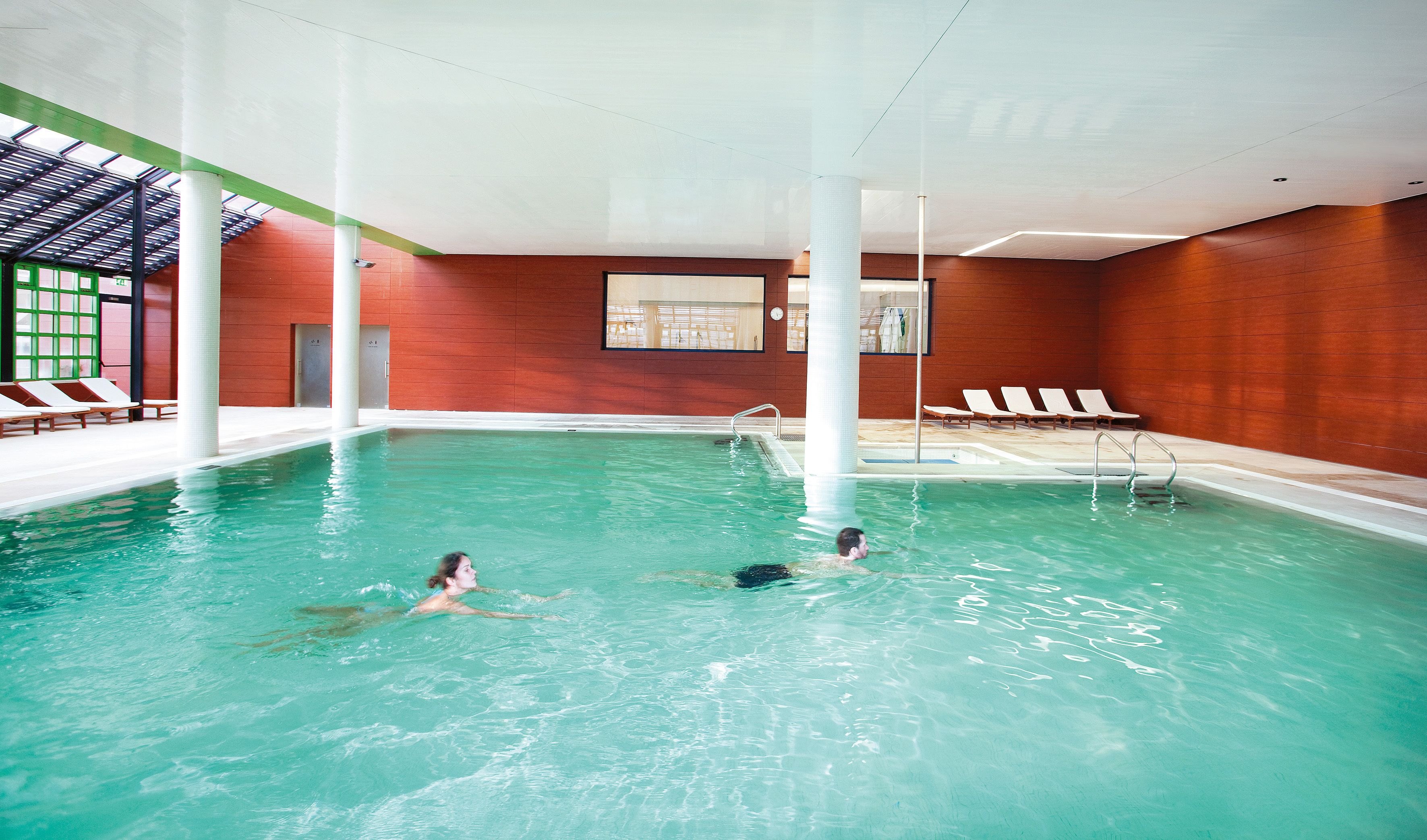 Una piscina interior con agua cristalina, sillones de descanso y un diseño moderno.