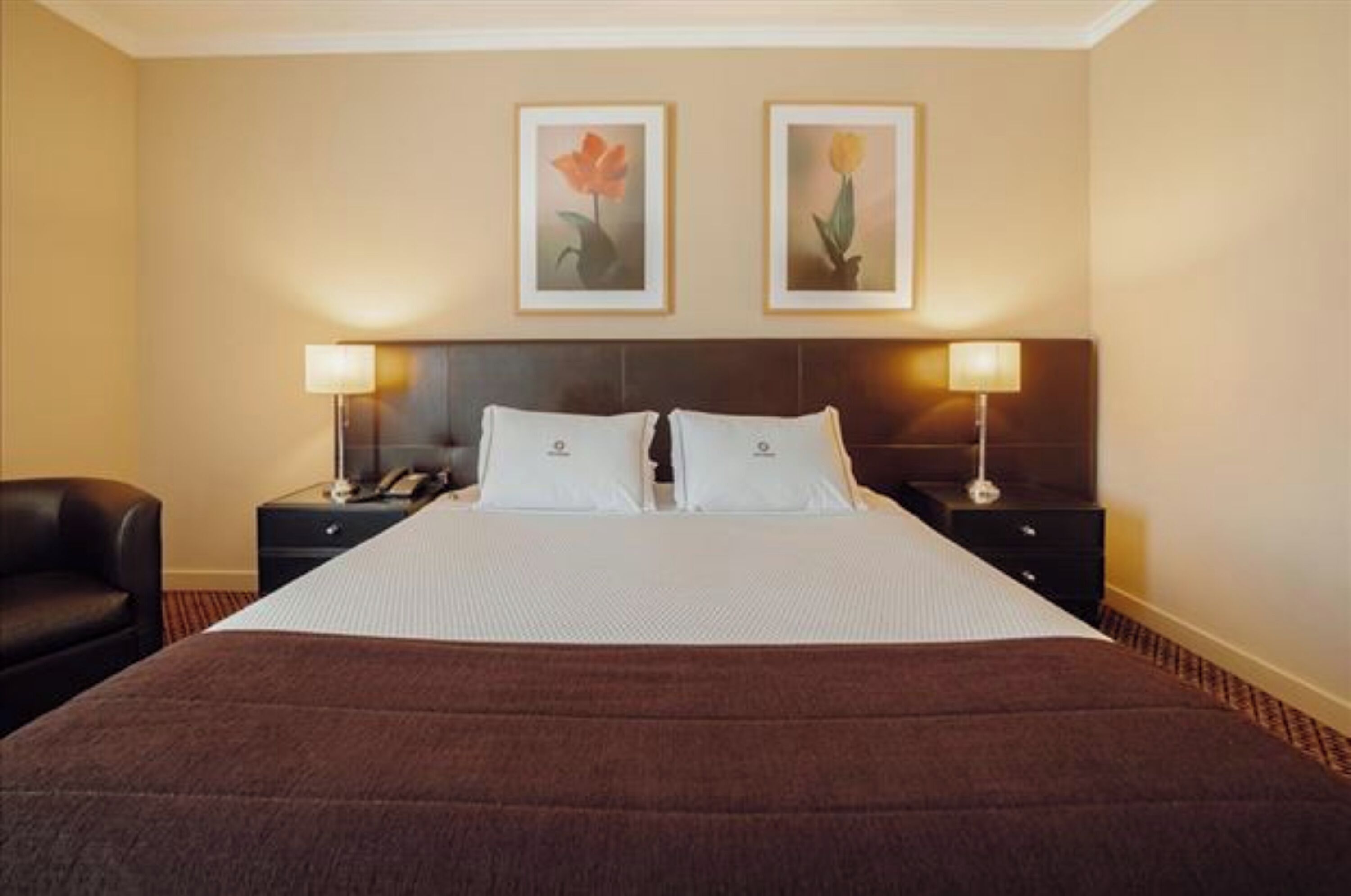 A hotel room with a large bed, two bedside tables with lamps, a chair, and two framed pictures on the wall.