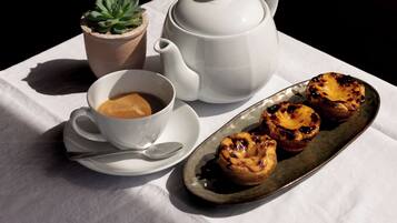 A table with a white tablecloth, a white teapot, a cup of coffee, a small potted plant, and a plate of pastries.
