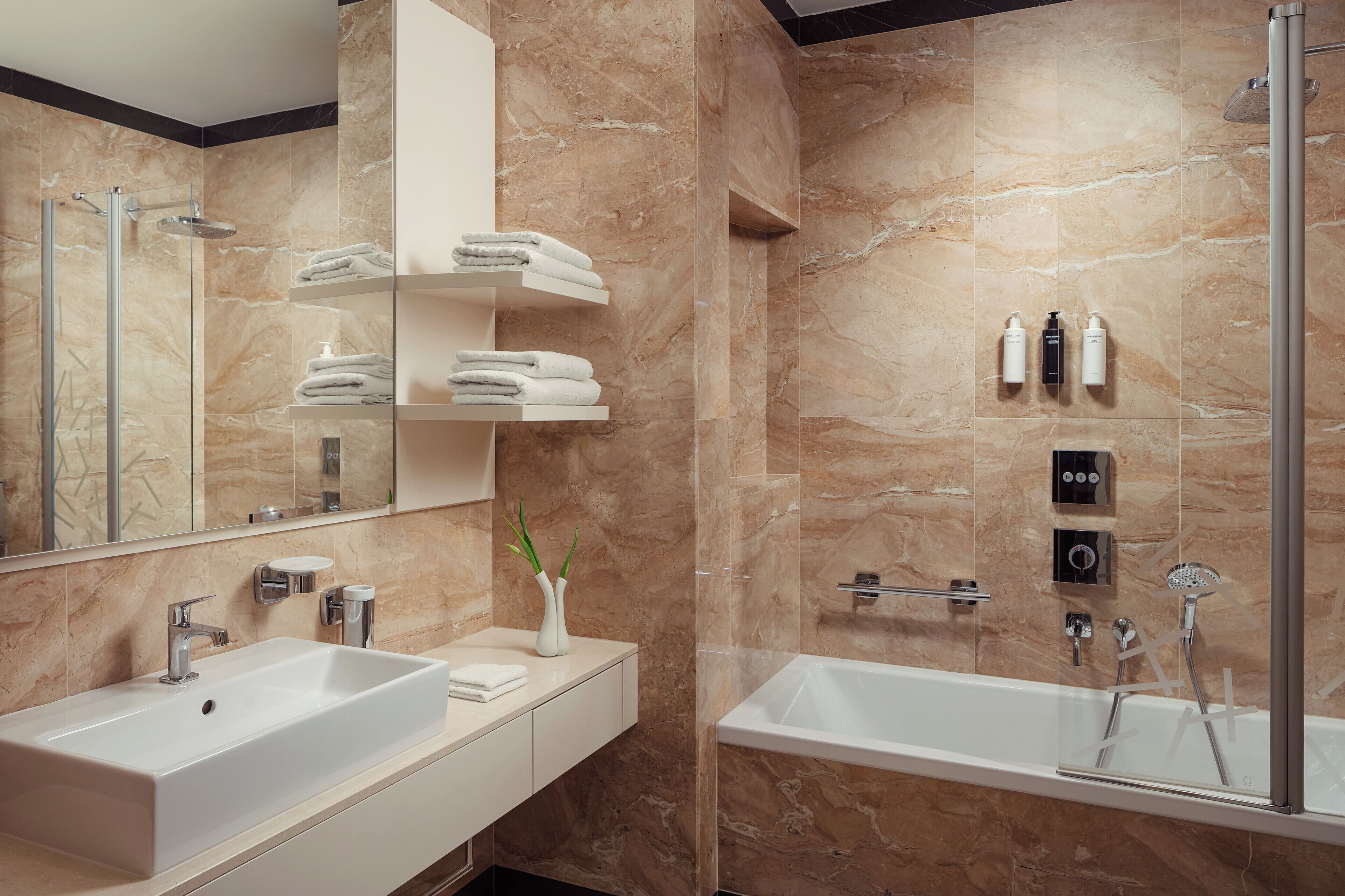 A modern bathroom with a large mirror, two sinks, a bathtub, and a shower area.