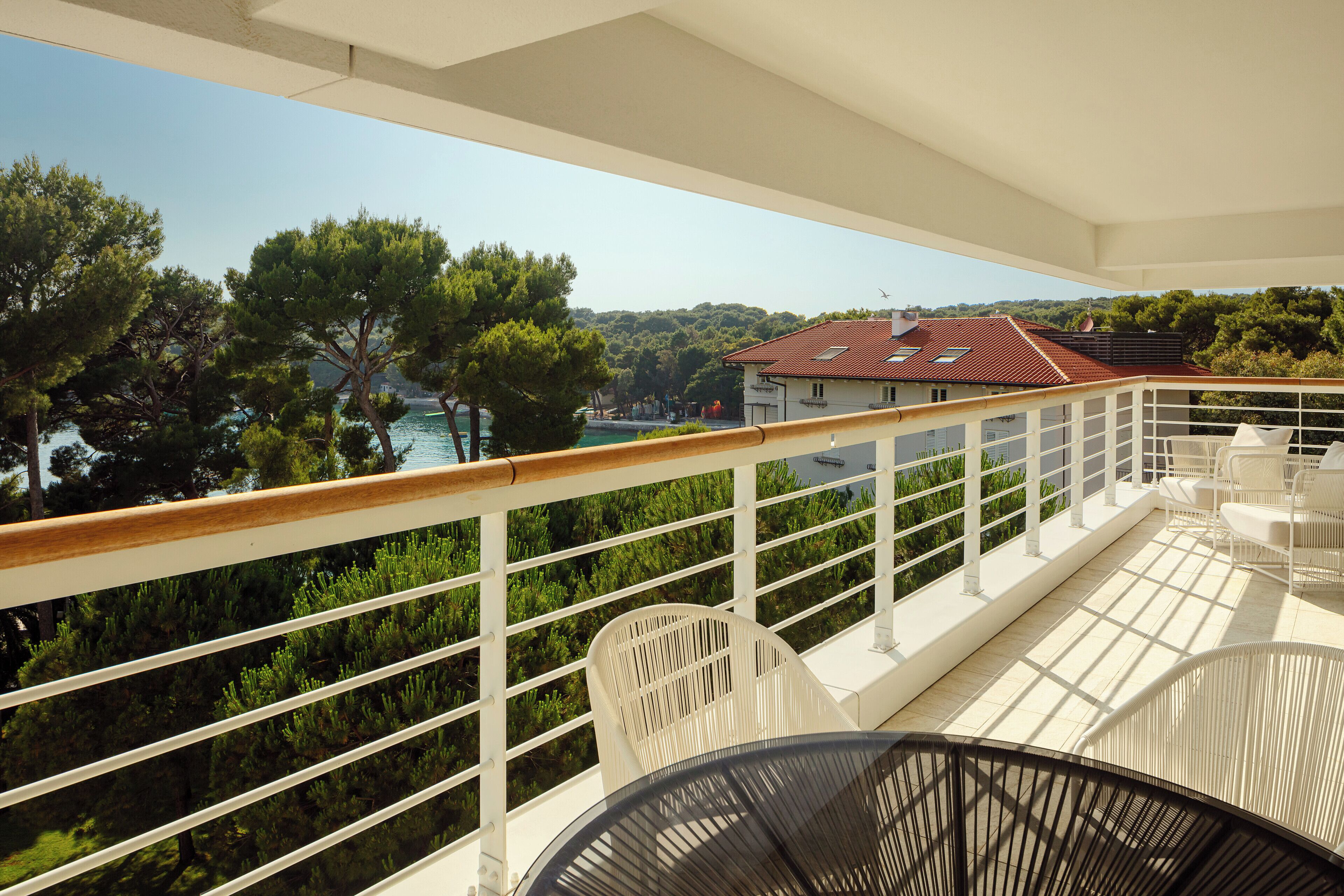 A balcony with white railings, a wooden deck, and a view of a coastal area with trees and buildings.