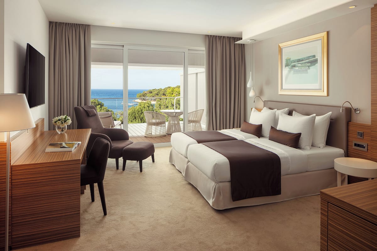 Ein Hotelzimmer mit einem großen Bett, einem Schreibtisch mit Stuhl, einem Fernseher und einem Balkon mit Meerblick.