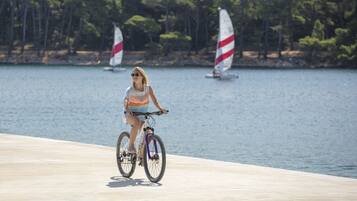 A person riding a bicycle on a concrete path by a body of water with sailboats in the background.