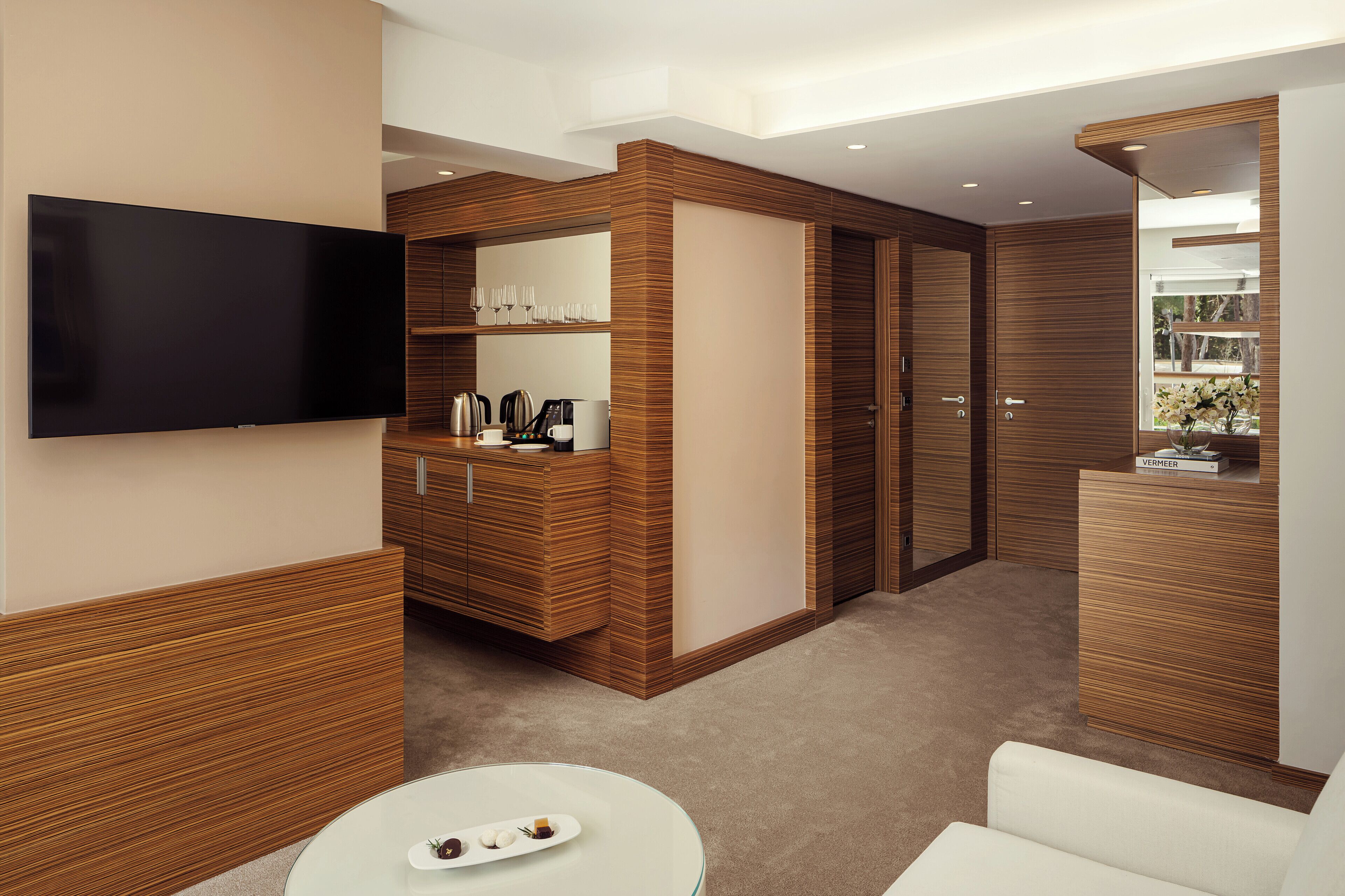 A modern living room with a flat-screen TV, wooden cabinetry, a glass coffee table, and a sofa.