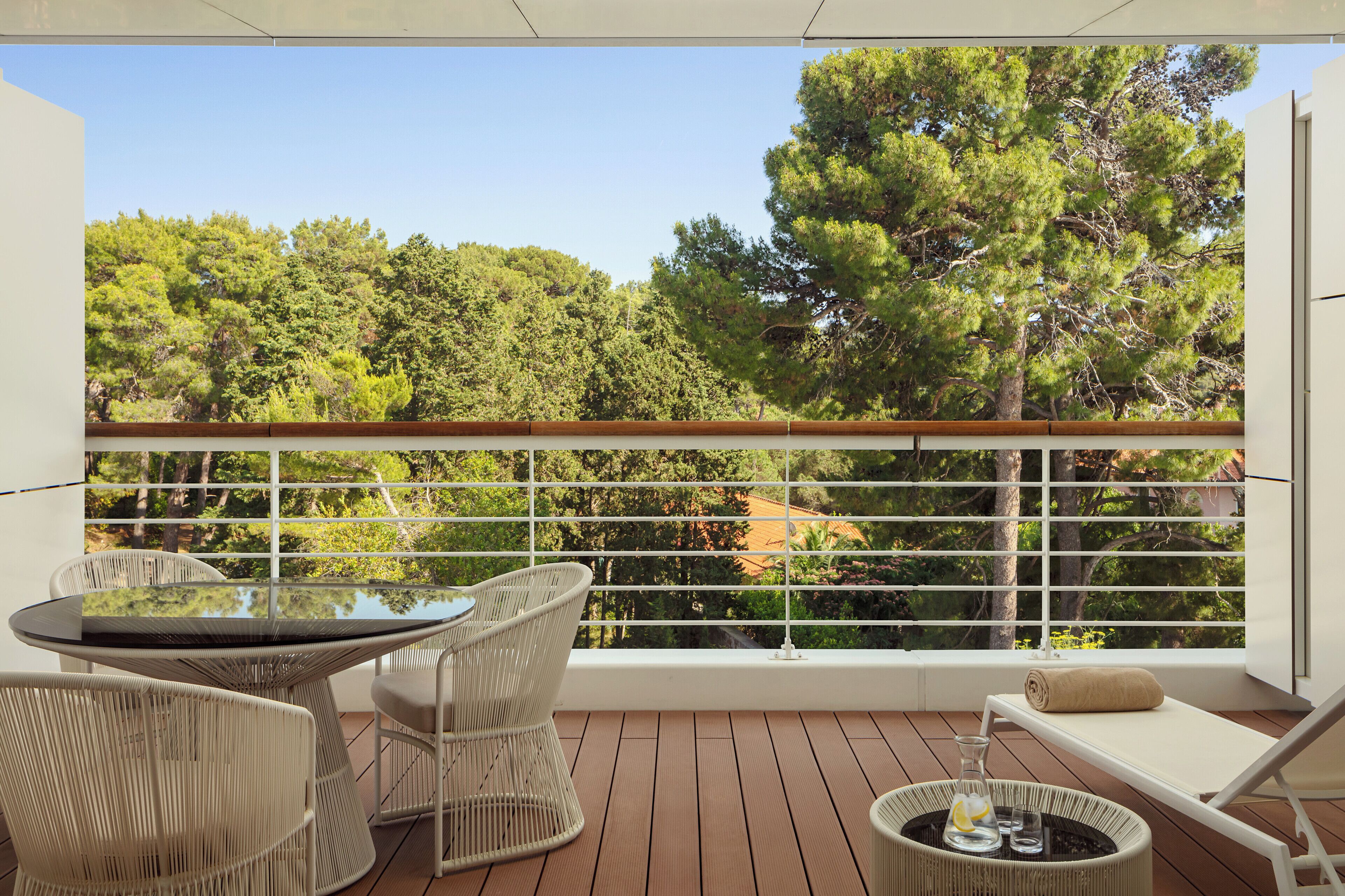 A balcony with a table and chairs, a cushioned seat, and a view of trees.