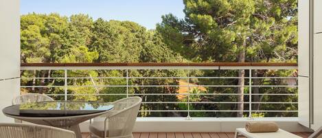 A balcony with a table and chairs, a cushioned seat, and a view of trees.