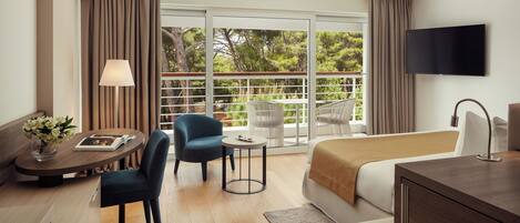 Une chambre d’hôtel avec un lit, un bureau, une chaise, une télévision et un balcon donnant sur la verdure.