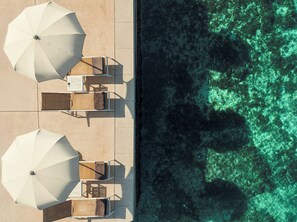 Vista aérea de un resort frente a la playa, con tumbonas y sombrillas, una piscina y agua turquesa cristalina.