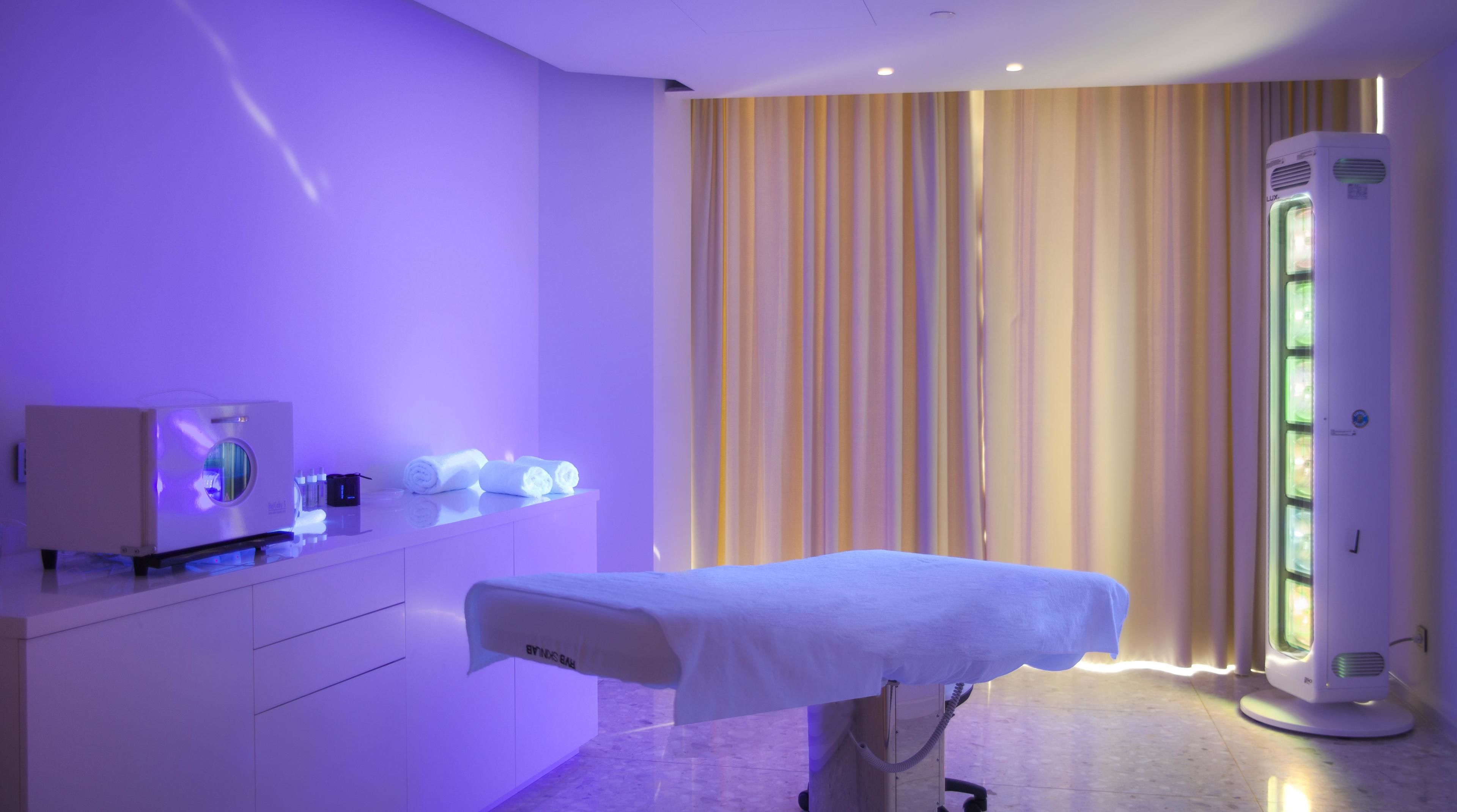 Een medische behandelkamer met een behandeld bed, een massagestoel en een therapieapparaat aan de muur.