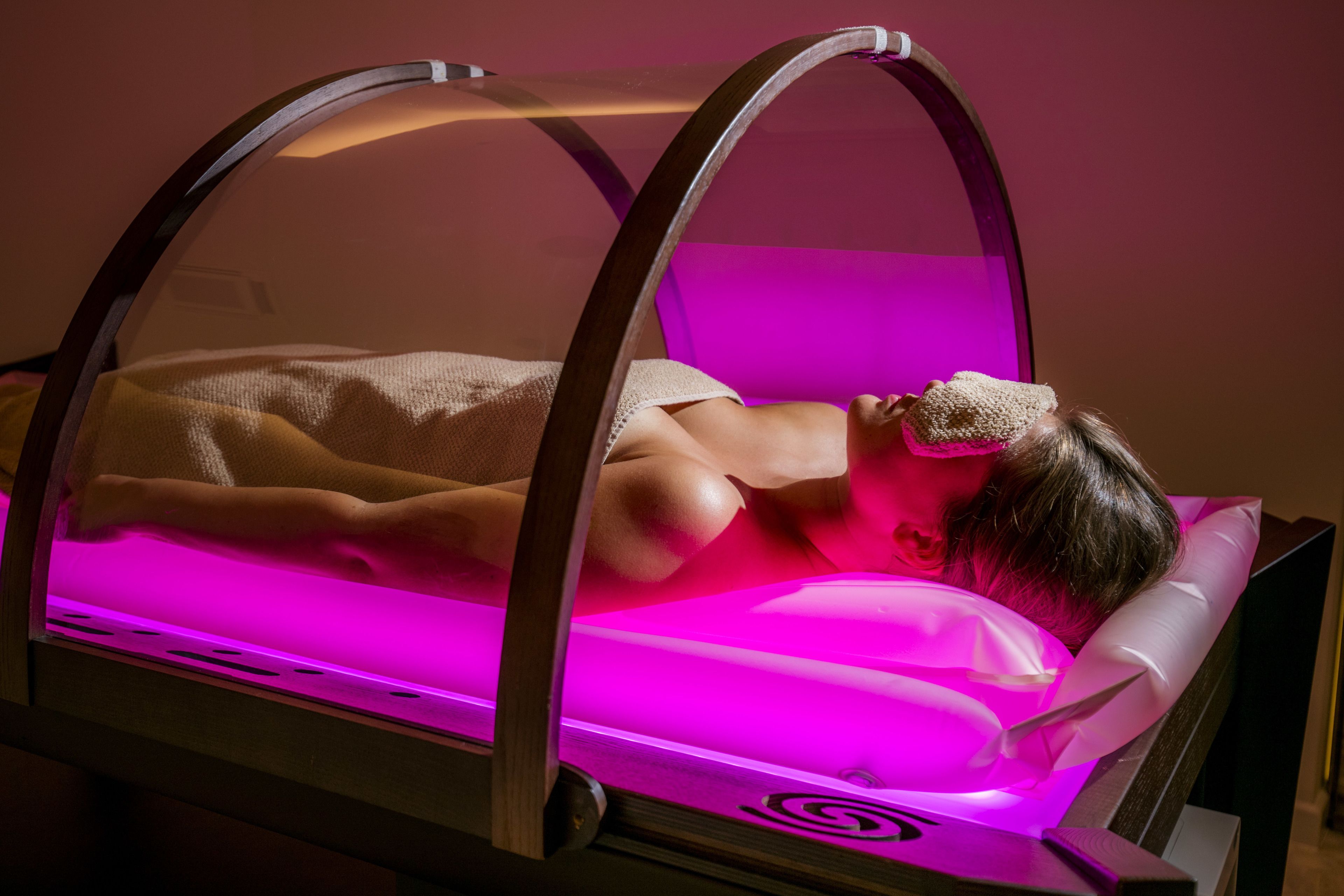 A person lying in a bed with a canopy, illuminated by pink lighting.